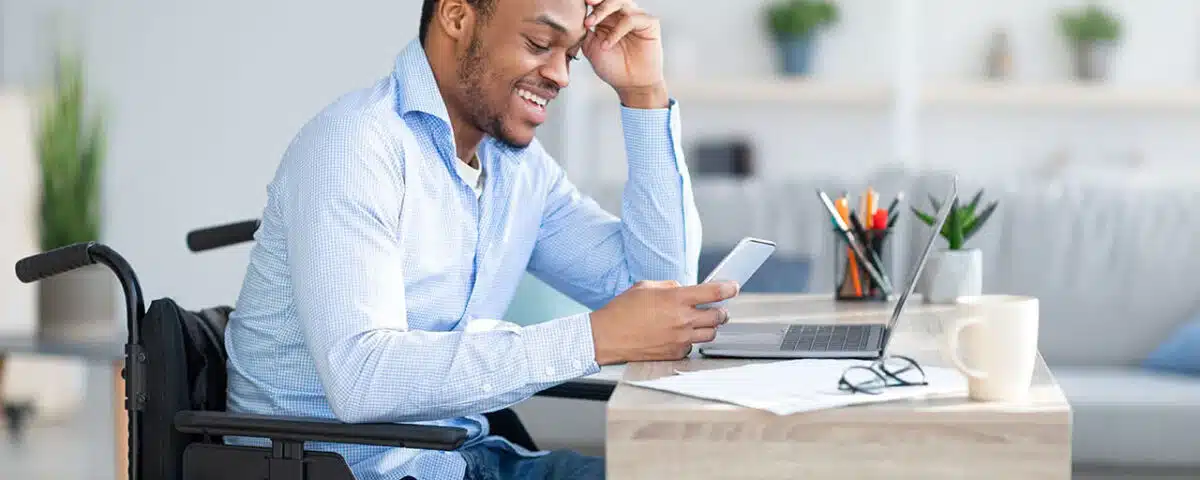 Man in wheelchair using cell phone and laptop