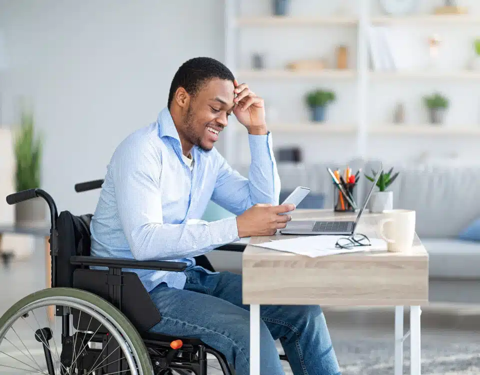 Man in wheelchair using cell phone and laptop